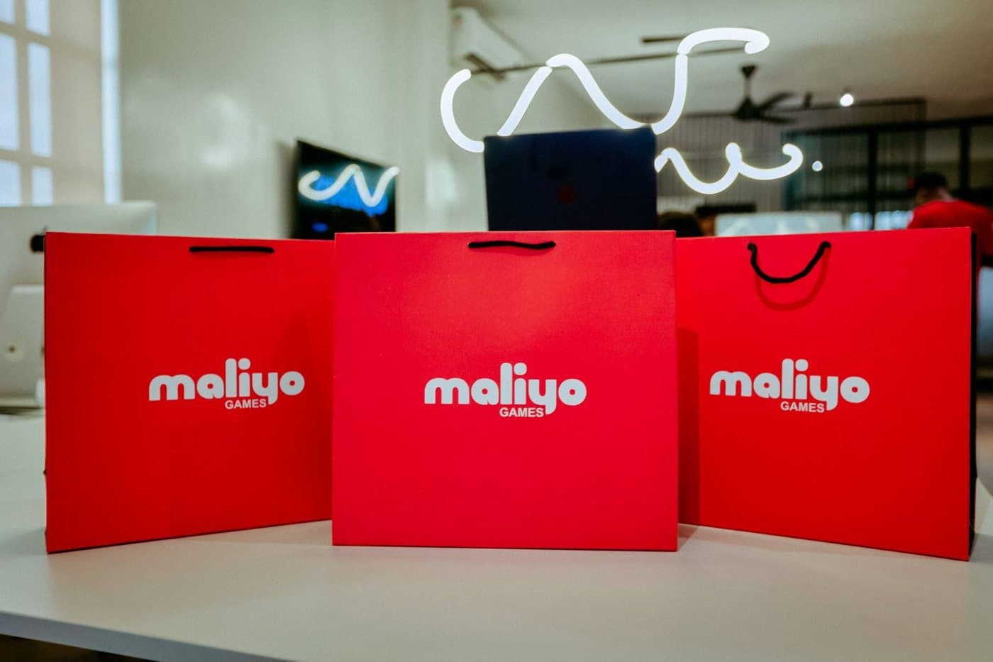 Three red Maliyo Games shopping bags on a table
